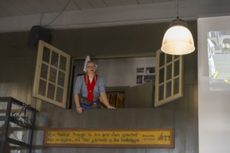 A woman in traditional traditional costume looks out of an open window in a room with traditional