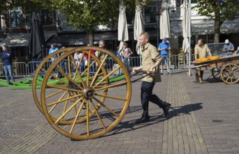 Man pushing large wooden cart wheel at a market in sunny weather, Wooden cart wheel for cheese