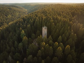 A tower surrounded by densely wooded hills catches the last rays of sunlight in the early evening,