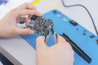 Person uses pliers to work on a circuit board surrounded by electronic parts