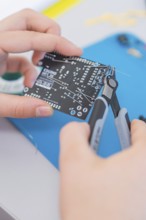 Person holds a circuit board and works on it with pliers on a blue mat