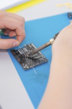 Person soldering an electronic circuit board with a soldering iron on a blue mat