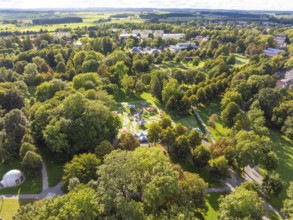Aerial view of a green park landscape with various trees and buildings in the background under a
