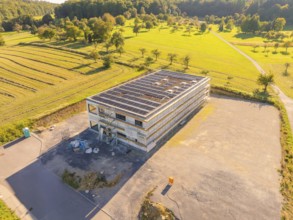 Building with solar panels, surrounded by landscape and fields, partly under construction, new