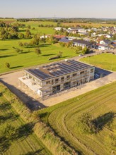 New building with solar panels on the roof, embedded in a green landscape near a village, new