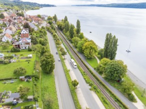 View of a town with road and railway tracks along a lake, surrounded by green areas, Lake Constance