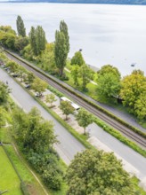 Road and parallel railway line next to a lake, surrounded by trees, Lake Constance Germany