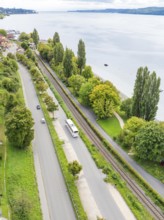 Aerial view of a road and railway line along a lake with trees and buildings, Lake Constance