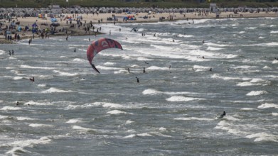 Kitesurfers and holidaymakers on the beach and in the sea, waves, beach chairs in the background,