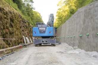 Blue excavator on a construction site between wooded earth slopes, Hermann Hessebahn construction