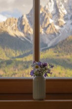A vase with meadow flowers stands on the windowsill in the background the mountains of the