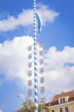 Bavarian maypole with coat of arms in front of blue sky and roof gable, Munich, Germany