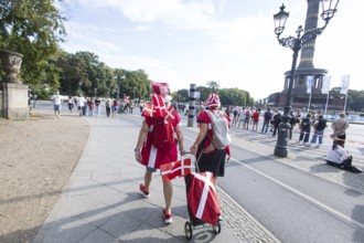 Two people carrying Danish flags run next to the Victory Column at the Großer Stern at the 51st BMW