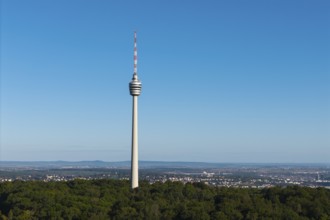 Detailed view of a television tower, embedded in forests, with a wide view of the city under a blue