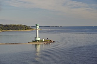 A lighthouse stands on a small headland in the calm sea under a slightly cloudy sky, Kiel Fjord,