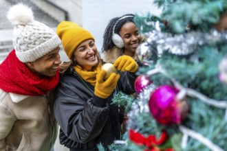 Group of cheerful multi ethnic friends decorating a christmas tree in the city, enjoying winter
