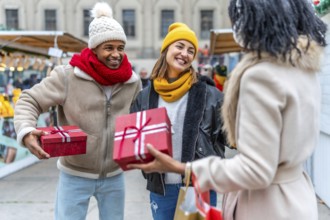 Happy friends exchanging christmas gifts at a bustling market, enjoying the festive atmosphere and