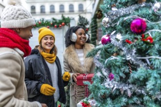 Three happy friends enjoying christmas shopping at an outdoor market, choosing a christmas tree and