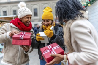 Happy multiethnic friends exchanging christmas gifts at a christmas market in the city center