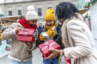 Three happy friends opening christmas gifts at a christmas market, enjoying winter holidays