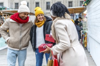 Happy friends exchanging christmas gifts while enjoying a stroll through a festive winter market