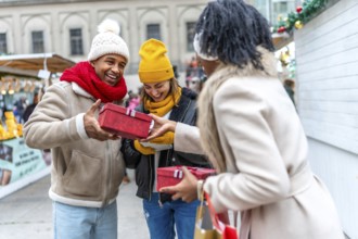 Happy multi ethnic friends exchanging christmas gifts at a christmas market, enjoying winter