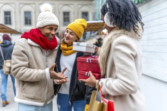 Three friends exchanging christmas gifts and shopping bags at a winter market, enjoying the festive