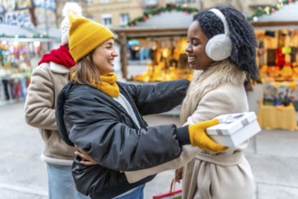 Two happy women exchanging christmas gifts at a christmas market, enjoying winter holidays together