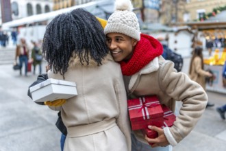 Two friends joyfully exchanging gifts at a bustling outdoor christmas market, surrounded by festive