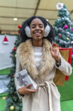 Happy customer holding a christmas present and shopping bags, enjoying winter sales in a decorated
