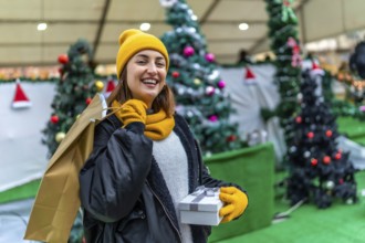 Smiling woman carrying shopping bags and gift box enjoying christmas shopping at a decorated