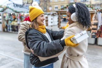 Two happy female friends exchanging christmas presents at a decorated outdoor city market during