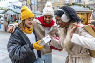 Three joyful friends exchanging gifts at a bustling christmas market, enjoying the festive