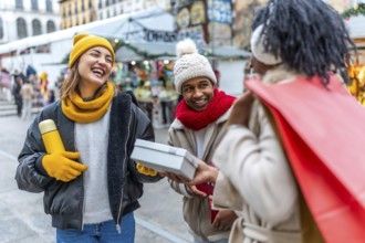 Happy multi ethnic friends joyfully exchanging christmas gifts at a bustling winter market,