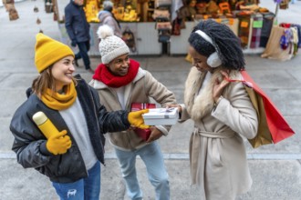 Happy multi ethnic friends joyfully exchanging christmas gifts while shopping together at a