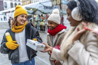 Happy multi ethnic friends exchanging christmas presents at a winter street market, enjoying the