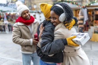 Happy friends exchanging christmas gifts and hugging at a christmas market during winter holidays