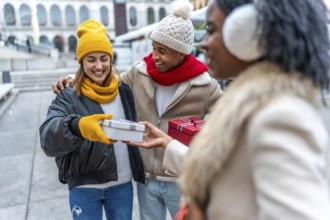 Happy multi ethnic friends joyfully exchanging christmas gifts in a bustling city, celebrating the