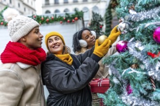Happy multi ethnic friends decorating christmas tree at outdoor christmas market, wearing winter