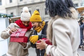 Happy friends joyfully exchanging christmas gifts at a bustling market, celebrating the festive