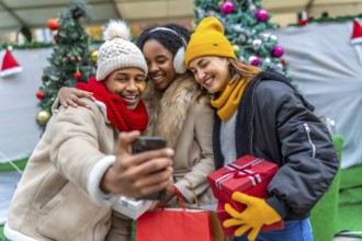 Group of cheerful multi ethnic friends taking a selfie with a smartphone after winter shopping at a