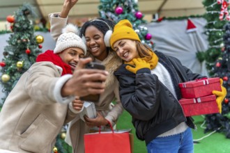 Happy multi ethnic friends taking a selfie after a christmas shopping spree, holding gifts and