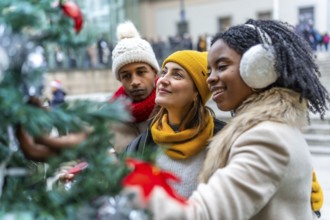 Three friends admiring christmas decorations on a city tree during winter holidays, enjoying time