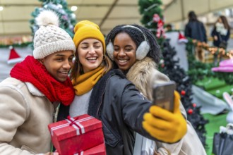 Happy multi ethnic friends taking a selfie at a christmas market, holding presents and shopping