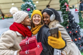 Happy multi ethnic friends taking a selfie at the christmas market, holding gifts and smiling