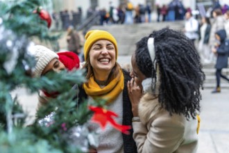 Three female friends are enjoying the christmas spirit, laughing near a decorated christmas tree in