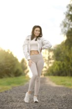 A playful woman stands on a gravel path, surrounded by lush greenery during golden hour