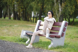A woman sits on a park bench, wearing leggings and a light jacket. She enjoys the warmth of calm