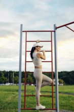 A woman in athletic wear engages in exercise on outdoor equipment. She showcases strength while