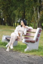A woman dressed in comfortable casual wear sits on a park bench, gazing thoughtfully into the
